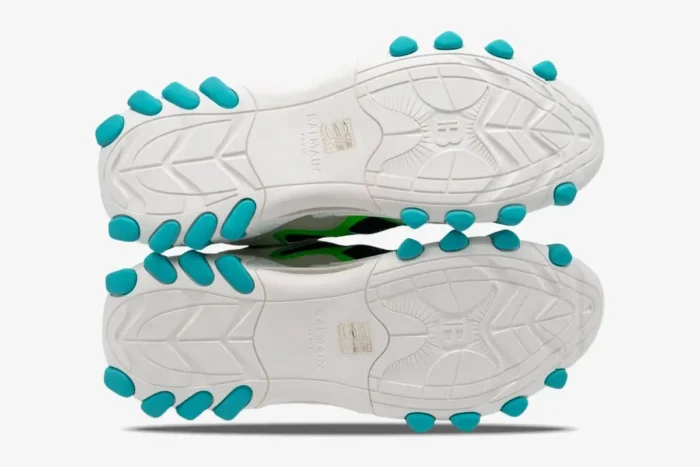 Bottom view of Balmain B-East sneakers showing white outsoles with turquoise rubber studs. - SKU AM1VI327THTF