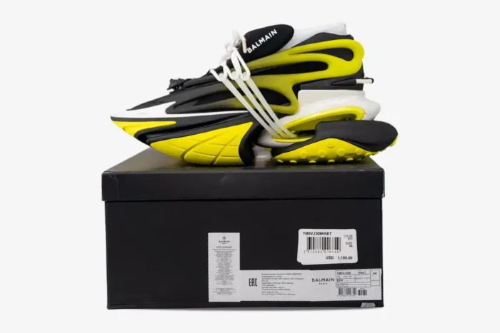 Balmain Unicorn low-top sneakers in black and yellow, side profile view on a black shoebox. - SKU YM0VJ309KNET