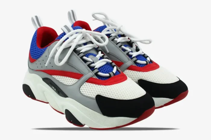 Dior B22 luxury sneakers in grey, red, and blue colorway, shown from a three-quarter side angle. - SKU 3SN231YKB_H865