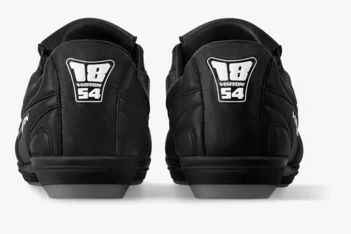 Rear view of black Louis Vuitton Footprint soccer shoes featuring the 18 VUITTON 54 logo on the heel.