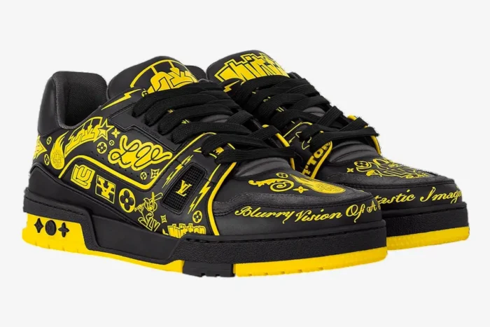 Black and yellow Louis Vuitton LV Trainer sneakers with graffiti graphics, three-quarter front view. - SKU 1A9JTV
