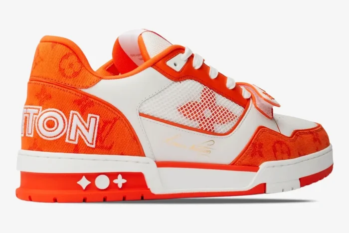 Side profile of a Louis Vuitton Trainer sneaker in orange monogram denim and white leather. - SKU 1A9ZBI