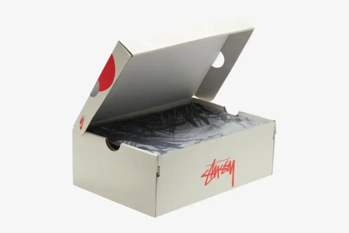 Off-white Nike x Stussy shoebox with red logos, open showing patterned tissue paper, three-quarter view. - SKU CZ9084-001