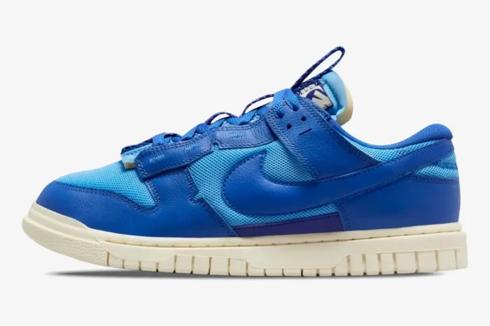 Side view of Nike Dunk Low Remastered Jumbo Blue sneakers with mixed blue mesh and leather overlays on a cream sole. - SKU DV0821-400