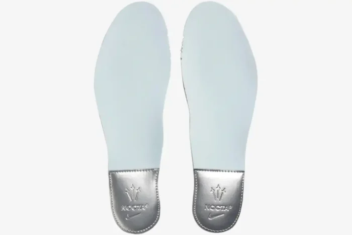 Top-down view of light blue Nike NOCTA Glide insoles featuring metallic silver heels with embossed branding. - SKU DM0879-001