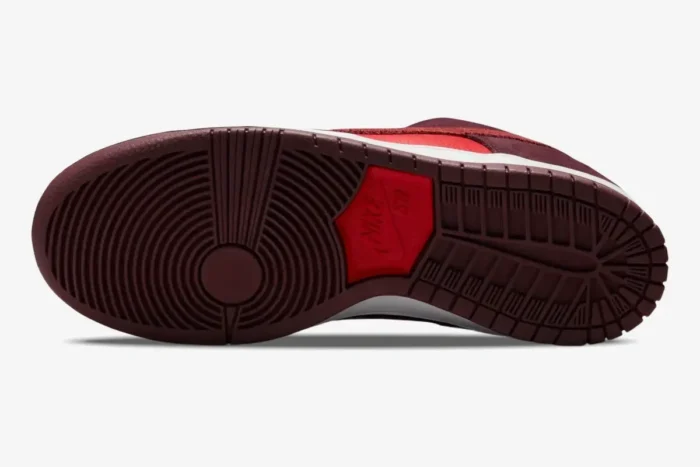 Bottom view of Nike SB Dunk Low Cherry showing burgundy outsole and red logo patch. - SKU DM0807-600