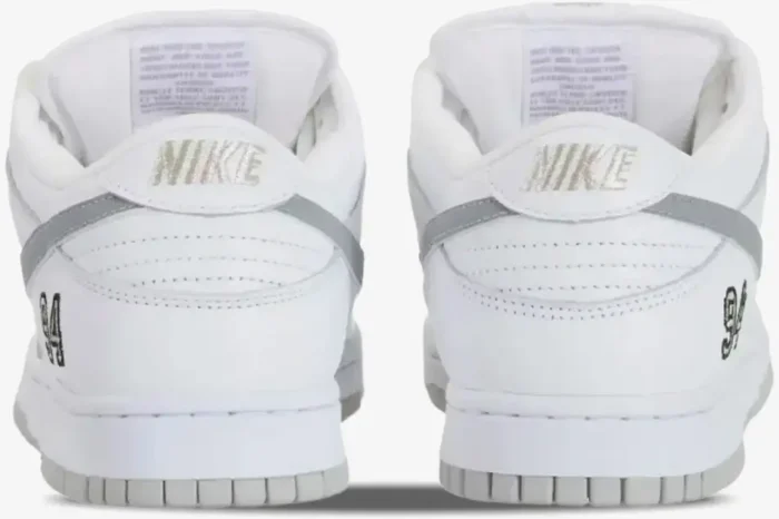 Rear view of Nike SB Dunk Low x Supreme sneakers in white and grey with silver heel embroidery and '94' logo. - SKU HQ8487100