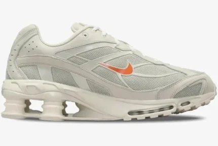Side profile of a Nike Shox Ride 2 sneaker in cream with an orange swoosh and visible heel columns. - SKU DJ5415-100