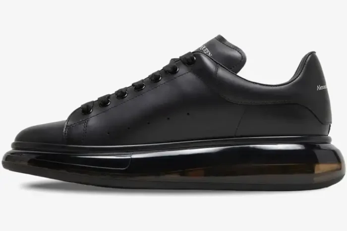Side profile of an Alexander McQueen black leather Oversized sneaker with a thick transparent sole. - SKU 604232-WHX98-1000