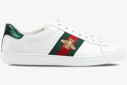 Side profile of white Gucci Ace leather sneakers with a gold embroidered bee and green and red web stripe. - SKU 42944602JP09064