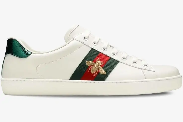 gucci-ace-bee-white-leather-sneaker-side-view-42944602jp09064-862-190 Side view of white Gucci Ace leather sneakers featuring a gold embroidered bee on a green and red web stripe. - SKU 42944602JP09064