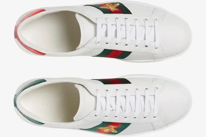 Top-down view of white Gucci Ace sneakers with gold bee embroidery and mismatched red and green heel tabs. - SKU 42944602JP09064